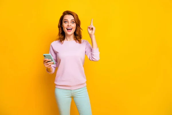 Eccellente Foto di bella signora tenere le mani del telefono hanno idea post creativo sollevare dito persona intelligente indossare pullover rosa pantaloni verdi isolato colore giallo sfondo — Foto Stock