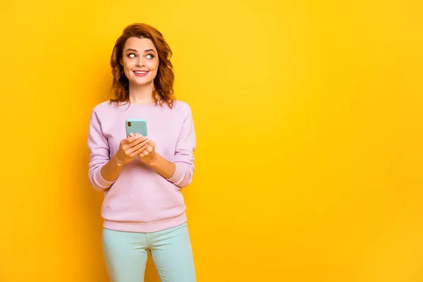 Foto van mooie dame houden telefoon moderne technologie kijken lege ruimte denken over nieuwe smart phone kopen slijtage roze trui groene broek geïsoleerde gele kleur achtergrond — Stockfoto