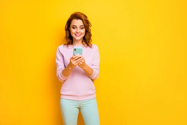 かなり面白い女性の写真を保持電話手現代的な技術のユーザーは、新しいスマートフォンモデルをしようとしてピンクのプルオーバー緑のパンツ孤立黄色の色の背景を着用 — ストック写真