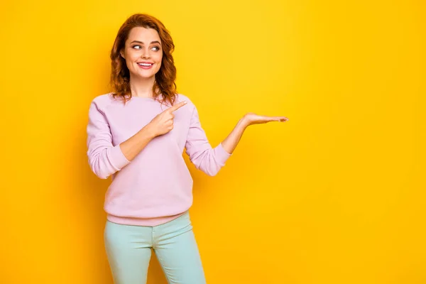 Φωτογραφία από αστεία κυρία κατέχουν καινοτομία υποδεικνύοντας προϊόν δάχτυλο σε ανοικτό βραχίονα συμβουλεύει την πώληση χαμηλές τιμές ψώνια φορούν ροζ πουλόβερ πράσινο παντελόνι απομονωμένο κίτρινο χρώμα φόντο — Φωτογραφία Αρχείου