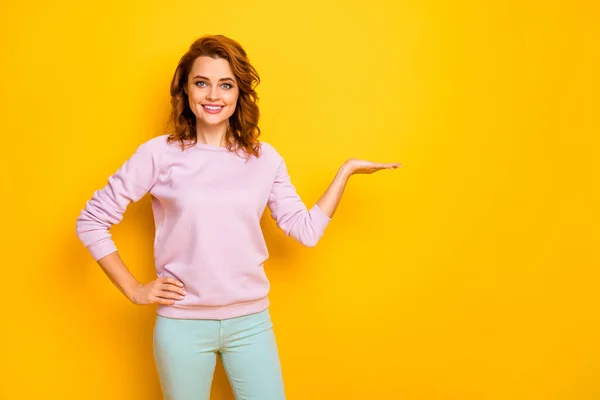 Foto van grappige positieve dame houden nieuwigheid product op open palm arm adviseren verkoop lage prijzen winkelen dragen roze trui groene broek geïsoleerde gele kleur achtergrond — Stockfoto