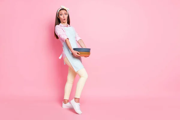 Portrét ohromený frustrovaný dívka manželka držet mnoho nádobí potřebují umýt dojem nosit košili kalhoty boty izolované přes pastelové barvy pozadí — Stock fotografie