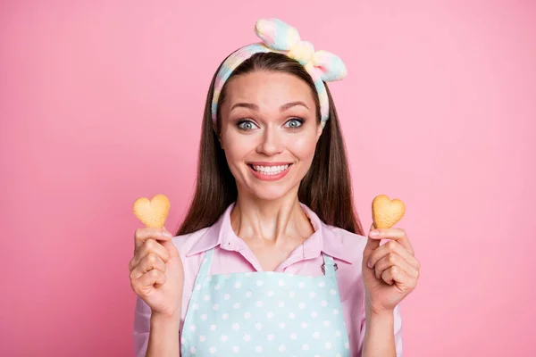 Close-up portrait of her she nice attractive cheerful cheery hungry funky brown-haired housewife holding in hands fresh cookies heart form shape isolated on pink pastel color background — Stock Photo, Image