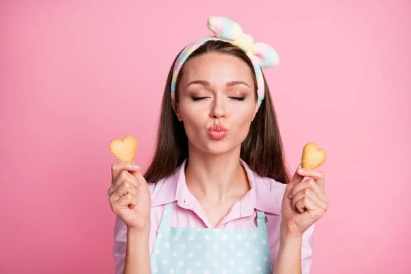 Close-up portrait of her she nice attractive dreamy affectionate brown-haired housewife holding in hands fresh tasty yummy cookies heart form sending air kiss isolated on pink pastel color background — Stock Photo, Image
