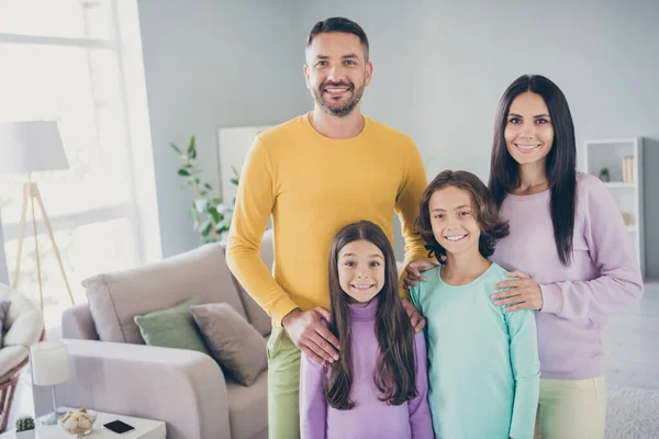 Foto de família grande quatro pessoas reunindo duas crianças pequenas mãos ombros usam calças de camisola coloridas na sala de estar dentro de casa — Fotografia de Stock