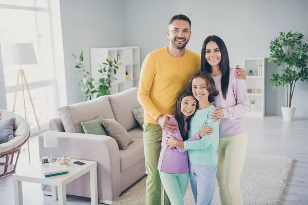 Foto van het hele gezin vier mensen ontmoeten twee kleine kinderen omarmen dragen kleurrijke trui broek in de woonkamer binnen — Stockfoto