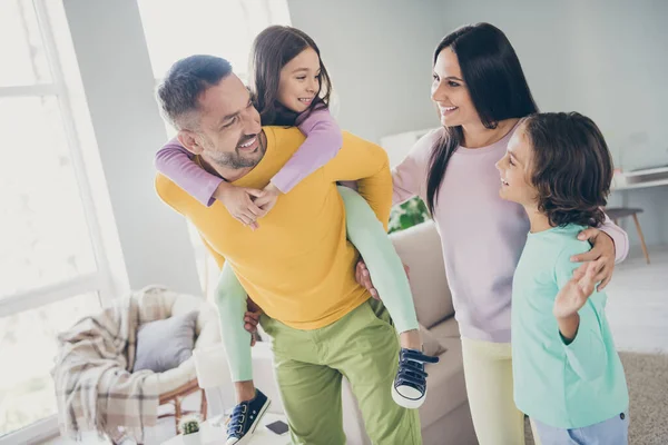 Foto av hela familjen fyra personer träffar två barn far håller gris rygg dotter bära färgglada jumper byxor i vardagsrummet inomhus — Stockfoto