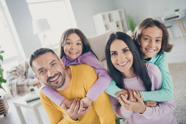 Zdjęcie pełnej rodziny czterech ludzi rodzice trzymać świnkę z powrotem dzieci noszą kolorowy sweter w salonie w pomieszczeniach — Zdjęcie stockowe