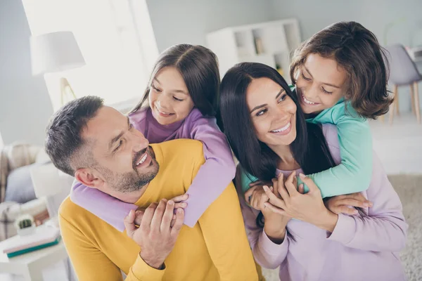 Foto van grote familie vier leden ouders houden piggy back kinderen kijken ogen dragen kleurrijke trui in de woonkamer binnen — Stockfoto
