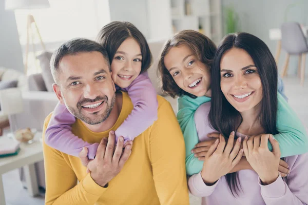 全家人的照片四个人父母抱着小猪背收养的孩子闪亮的微笑相机在客厅里穿着五颜六色的毛衣 — 图库照片