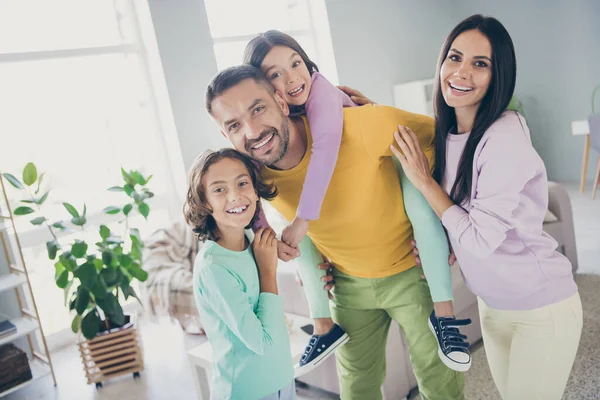 Foto av hela stora familjen fyra personer pappa håller gris rygg dotter krama släktingar bär färgglada tröja byxor i vardagsrummet inomhus — Stockfoto