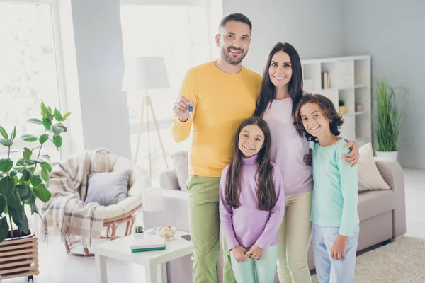 Fotografie celé rodiny čtyři lidé objetí táta držet show klíče nosit barevné svetr kalhoty v obývacím pokoji uvnitř — Stock fotografie