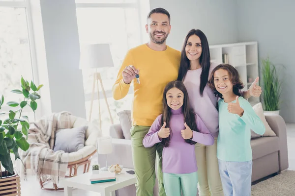 Foto van grote familie vier mensen heffen duim omhoog vader hold demonstreren sleutels dragen kleurrijke trui broek in de woonkamer binnen — Stockfoto