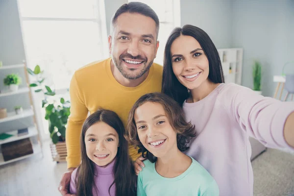 Foto de familia completa cuatro personas mami tomar selfie abrazo radiante sonrisa usar suéter de colores en la sala de estar en interiores —  Fotos de Stock