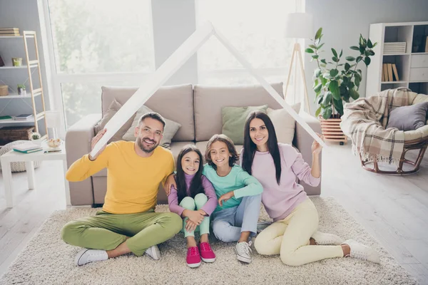 Foto da família completa quatro membros dois filhos pequenos pais seguram telhado sentar chão desgaste camisola colorida na sala de estar dentro de casa — Fotografia de Stock