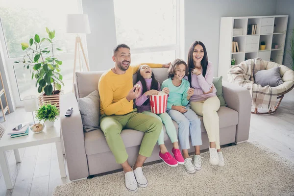 Foto de família cheia quatro pessoas sentar sofá comer milho pop assistir tv rir usar calças de camisola coloridas na sala de estar dentro de casa — Fotografia de Stock