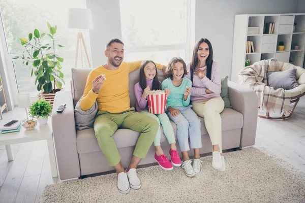 Foto de grande família completa quatro membros sentar sofá comer milho pop assistir série de comédia rir usar calças jumper coloridas na sala de estar dentro de casa — Fotografia de Stock