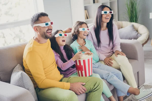 Фото большой семьи четыре человека сидят диван едят поп-кукурузу смотреть фильм носить 3D очки красочные брюки свитер в гостиной в помещении — стоковое фото