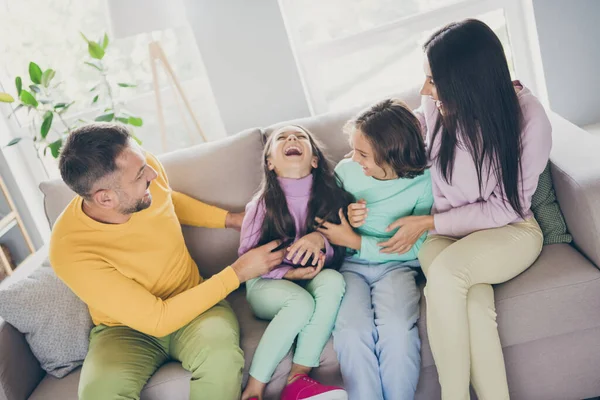 Foto der großen Familie vier Mitglieder sitzen Couch Papa kitzeln Tochter tragen bunte Pullover Hose im Wohnzimmer drinnen — Stockfoto