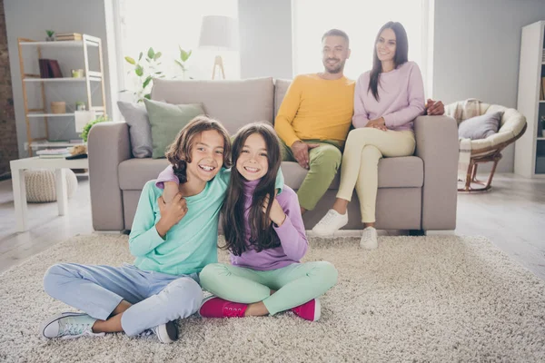 Foto van het hele gezin vier leden zitten sofa vloer twee kleine kinderen knuffel dragen kleurrijke trui broek in de woonkamer binnen — Stockfoto