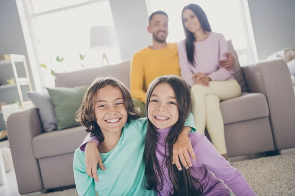 Foto van het hele gezin vier leden zitten op de bank tapijt twee kleine kinderen tweeling omarmen dragen kleurrijke trui broek in de woonkamer binnen — Stockfoto