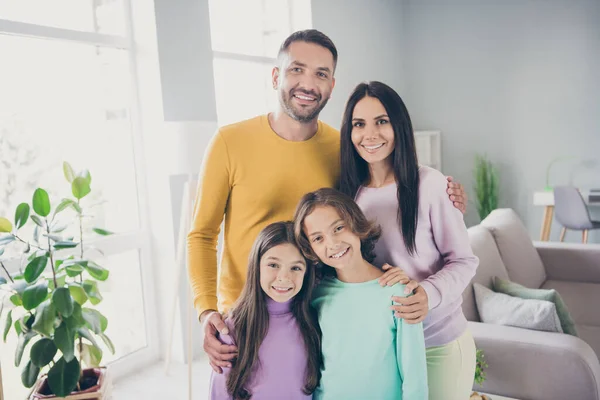 Foto de família completa quatro membros duas crianças pequenas abraçar sorriso brilhante desgaste pulôver colorido na sala de estar dentro de casa — Fotografia de Stock