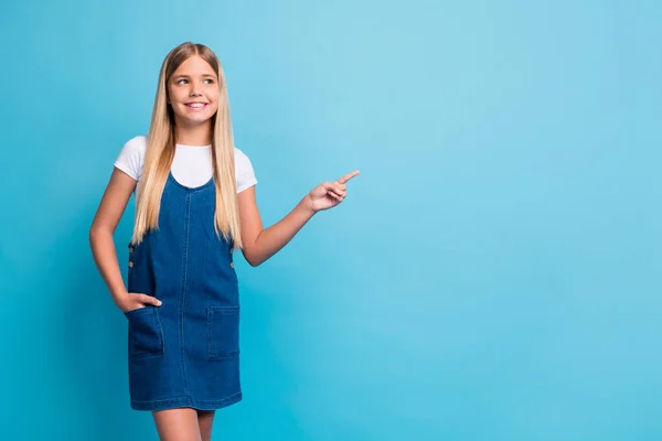 Foto em tamanho completo de alegre bonito adolescente loiro ponto da menina olhar espaço vazio desgaste branco t-shirt vestido de ganga isolado no fundo de cor azul — Fotografia de Stock