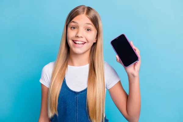 Retrato de optimista chica adolescente bonita mostrar teléfono anuncian desgaste casual mirada aislada sobre fondo de color azul pastel — Foto de Stock