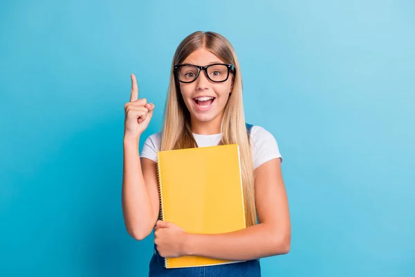 Foto de engraçado positivo loiro cabelo menina tem ideia apontando para cima desgaste óculos segurar livro isolado no fundo de cor azul — Fotografia de Stock