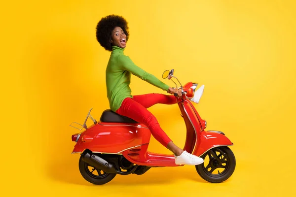 다리를 펼치고 빨간 스쿠터를 운전하고 있는, 흥분 한 흑인 여성의 사진, 선명 한 노란색 배경에 고립 된 평범 한 의상을 입고 있는 모습 — 스톡 사진