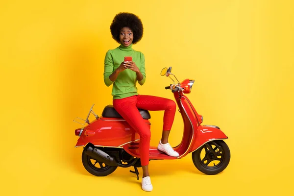 밝은 노란색 배경에 고립 된 단정 한 옷을 입은 채빨간 오토바이를 타고 흥분 한 젊은 여성의 사진 — 스톡 사진