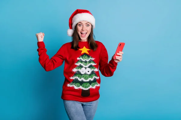 Photo of pretty cute lady fist up open mouth excited hold telephone wear santa x-mas headwear red ornamented sweater jeans isolated blue color background — Stock Photo, Image