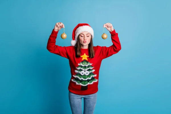 Portrait photo of girl wearing xmas jumper and headwear keeping showing decorative golden christmas balls baubles with plump pouted lips sending air kiss isolated on blue color background — Stock Photo, Image