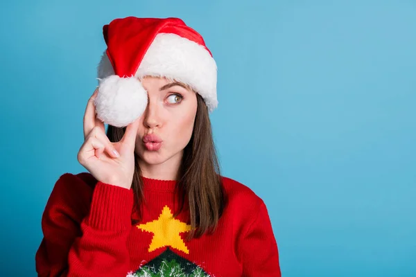 Foto de retrato de una joven milenaria con gorra de navidad sosteniendo una bola blanca de algodón suave en la mano mirando hacia un lado con labios rellenos de pucheros enviando un beso de aire aislado sobre un fondo de color azul. — Foto de Stock