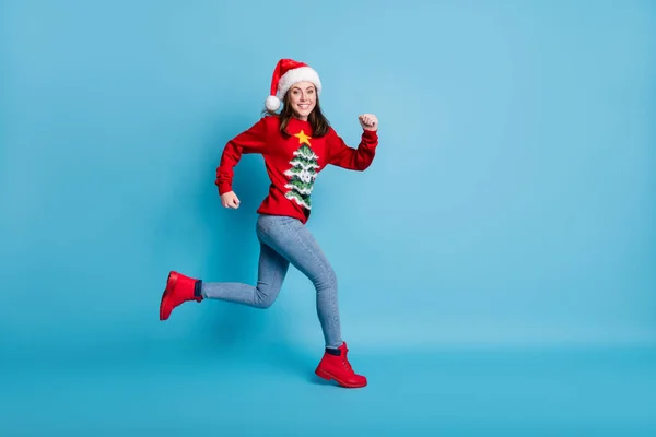 Повний розмір тіла фотографія профілю милої милої леді біжить хвилясті руки носити Санта х-м головний убір червоний прикрашений светр джинси чоботи ізольовані синій колір фону — стокове фото