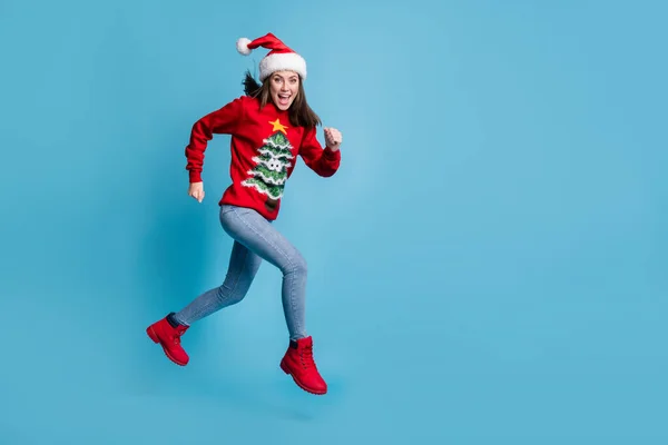 Foto de perfil de comprimento total de encantador bonito senhora salto sprinting ar aberto boca desgaste santa x-mas headwear vermelho ornamentado pulôver jeans botas isolado azul cor fundo — Fotografia de Stock