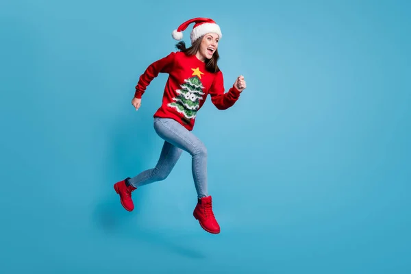 Full body size profile photo of cute lovely lady jump sprinting air hands fists open mouth wear santa x-mas headwear red ornamented pullover jeans boots isolated blue color background — Fotografia de Stock