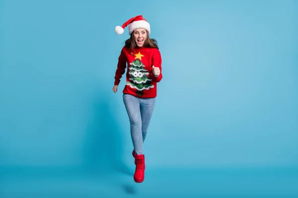 Full body size photo of charming cute lady jump fists running you excited open mouth wear santa x-mas headwear red ornamented pullover jeans boots isolated blue color background — Fotografia de Stock