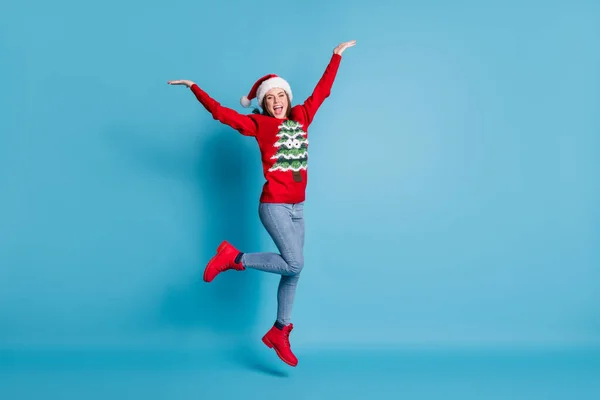 Повна довжина фотографії прекрасної красивої леді стрибати підняти руки долоні веселий відкритий рот носити Санта x-mas головні убори червоний прикрашений пуловер джинси чоботи ізольовані синій колір фону — стокове фото