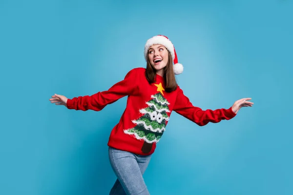 Photo of lovely cute lady excited look back empty space toothy beaming smile hands wear santa x-mas headwear red ornamented pullover jeans isolated blue color background — Stock Photo, Image