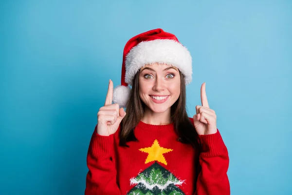 Foto de linda senhora bonita direta indicar dedos indicador espaço vazio animado sorriso usar santa x-mas headwear vermelho ornamentado pulôver isolado azul cor fundo — Fotografia de Stock