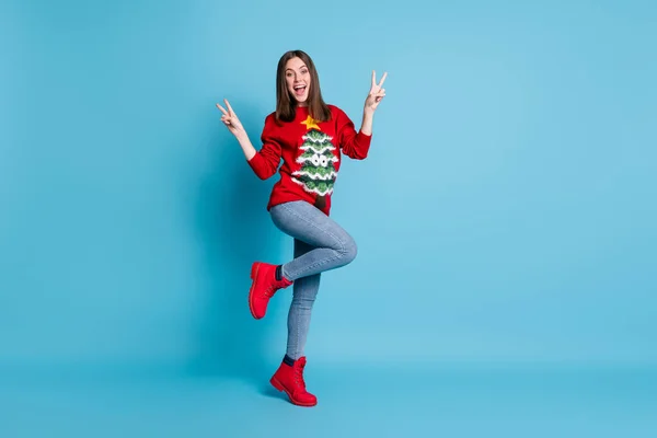 Pleine longueur taille du corps photo d'une fille portant rouge tenue de Noël jeans souriant montrant geste v-signe paix avec deux doigts isolés sur fond de couleur bleue — Photo