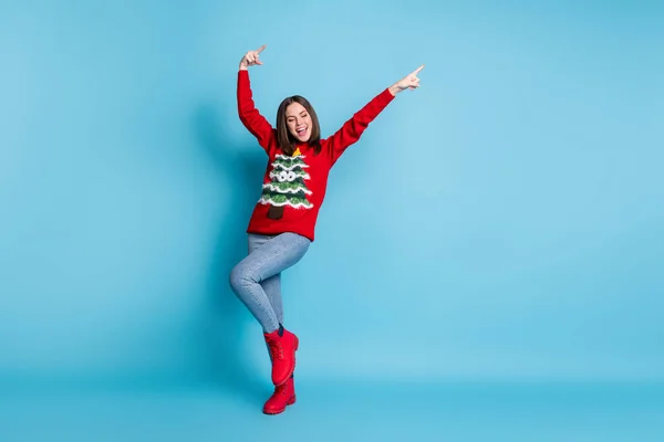 Photo portrait of happy brunette girl dancing smiling showing pointing up with fingers on both hands wearing red christmas sweater isolated on blue color background — Stock Photo, Image