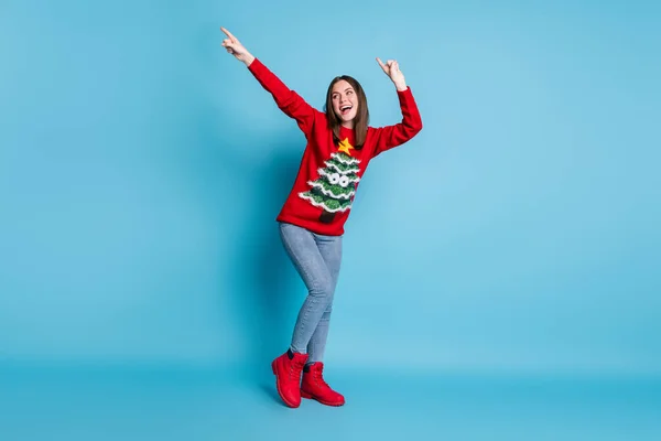 Photo portrait of pretty girl dancing smiling keeping hands over head showing pointing up with fingers wearing red christmas sweater isolated on blue color background — Stock Photo, Image