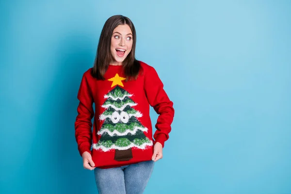 Photo portrait amazed young brunette woman showing sweater looking blank space smiling wearing denim pants red pullover with tree star googly eyes isolated on pastel light blue colored background — Stock Photo, Image
