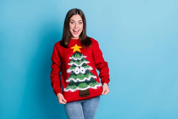 Photo portrait of smiling girl pulling sweater holding with hands smiling wearing jeans red pullover star googly eyes tree isolated on pastel light blue colored background with blank space — Stock Photo, Image