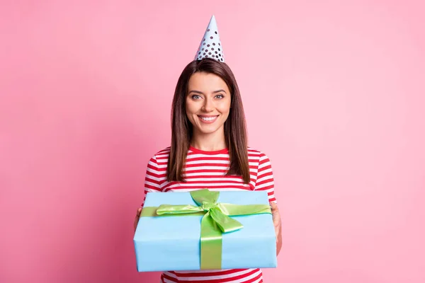Фотопортрет счастливой девушки, принимающей завернутый подарок в праздничной шляпе, весело улыбающейся изолированной на пастельно-розовом фоне — стоковое фото