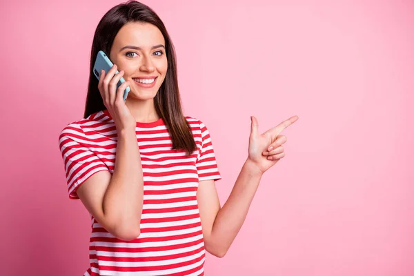 파스텔 핑크 색 배경에 고립 된 빈 공간을 손가락으로 가리키며 핸드폰으로 말하고 있는 놀란 여인의 사진 — 스톡 사진