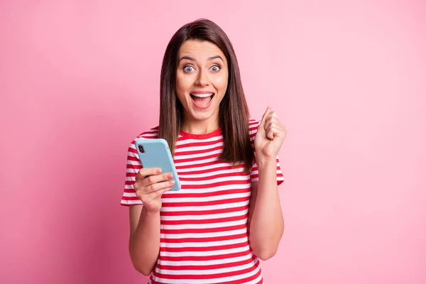 티셔츠 줄무늬 옷을 입고 있는 소녀의 사진 똑똑 한 전화가 파스텔 핑크 색 배경에 고립 된 우승자처럼 몸짓을 하고 있다 — 스톡 사진