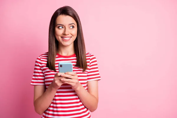 Foto de agradável engraçado jovem senhora segurar smartphone olhar espaço vazio desgaste listrado vermelho branco t-shirt isolado sobre pastel rosa fundo — Fotografia de Stock